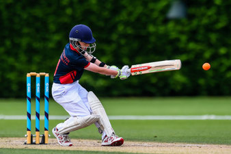 Boy in helmet and pads whacks a cricket ball