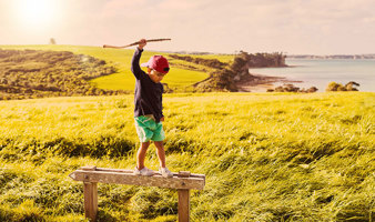 Young boy playing with a stick, balancing on a fence