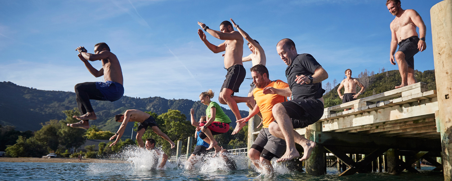 Men jumping off a jetty into the water on a sunny day