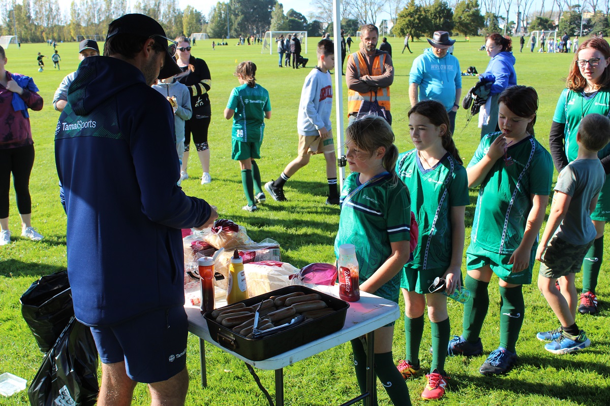 Tamariki waiting in line at a sausage sizzle